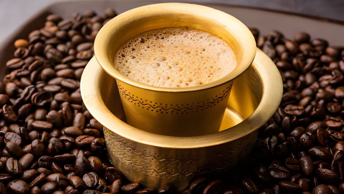Traditional brass cup of frothy filter coffee with beans