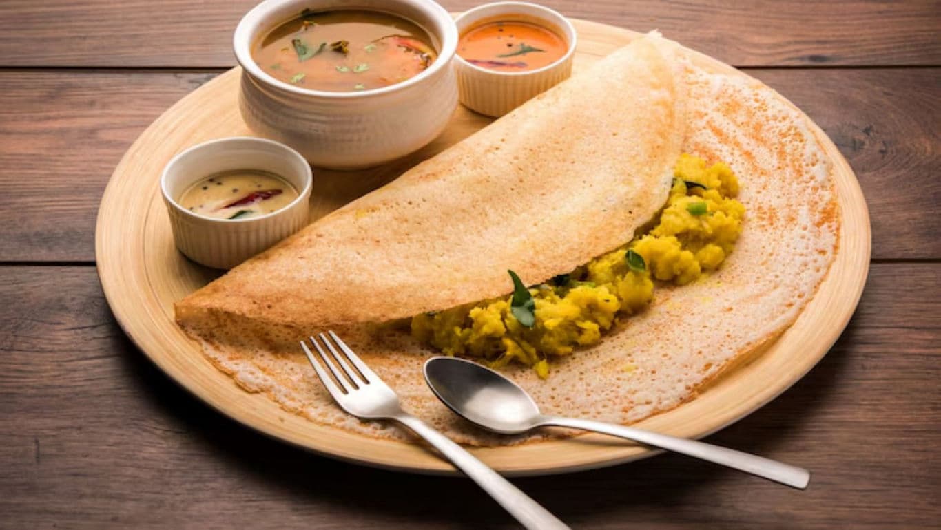 Masala dosa with sambar and chutneys on wooden table